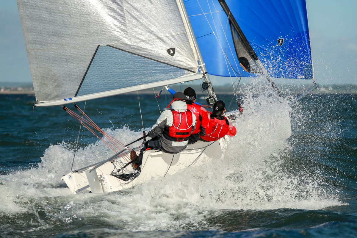 A crew racing a small sailboat through spray
