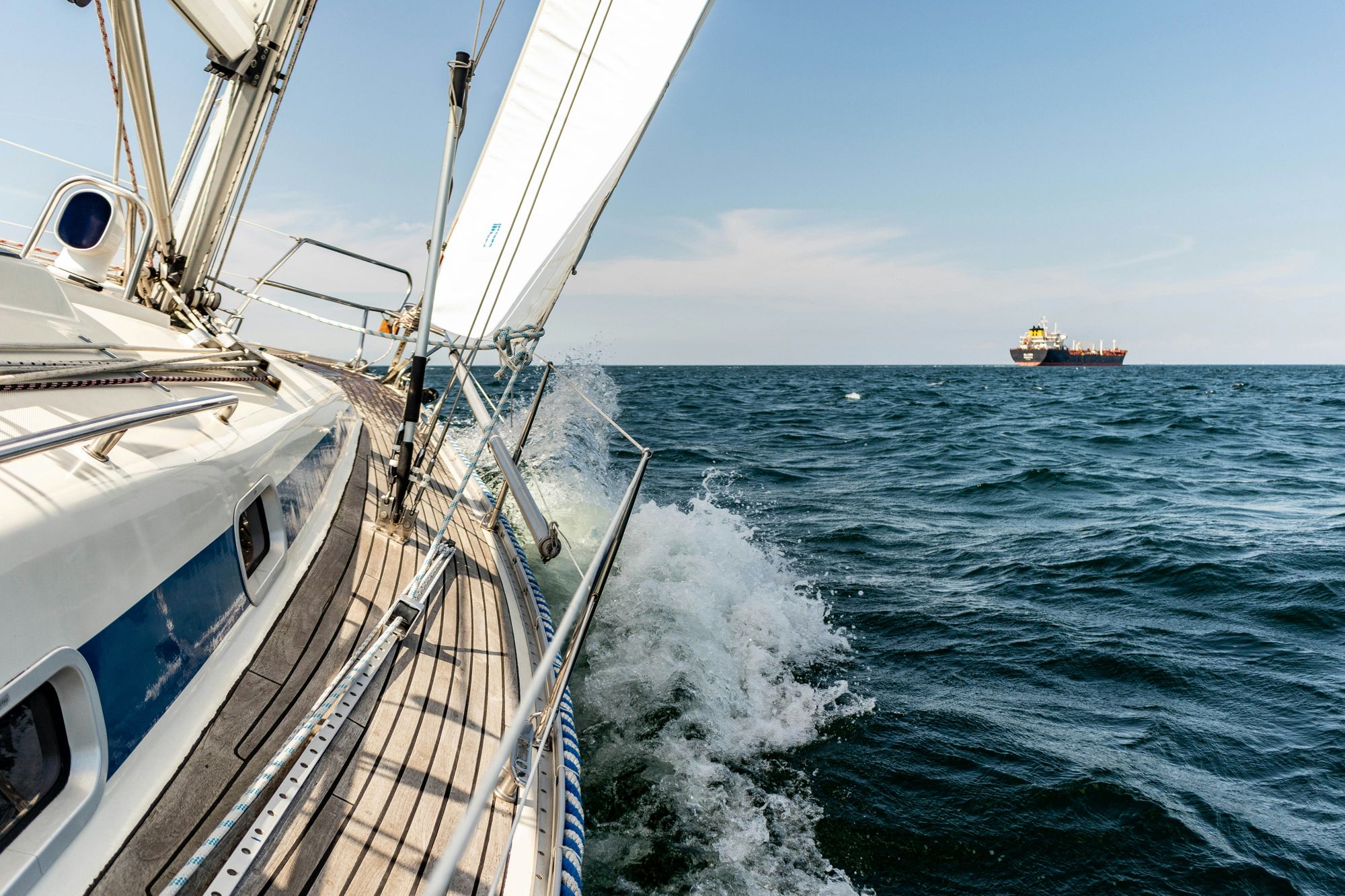 A sailboat heeling on open water with a ship on the horizon