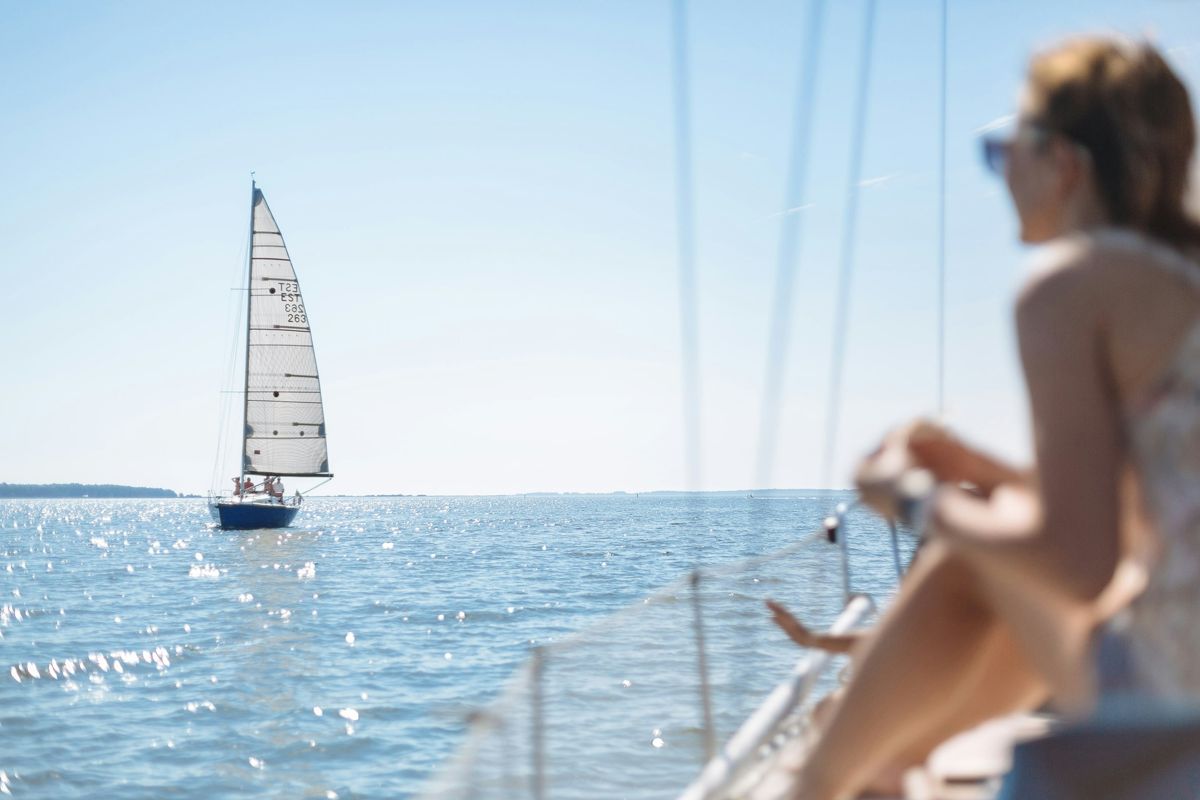 A sailor on deck watching another sailboat cross the bay