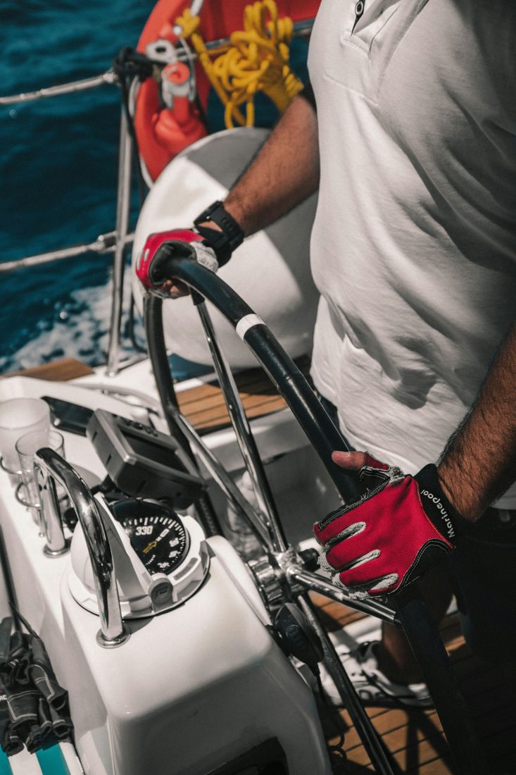 Hands in sailing gloves on the wheel of a sailboat