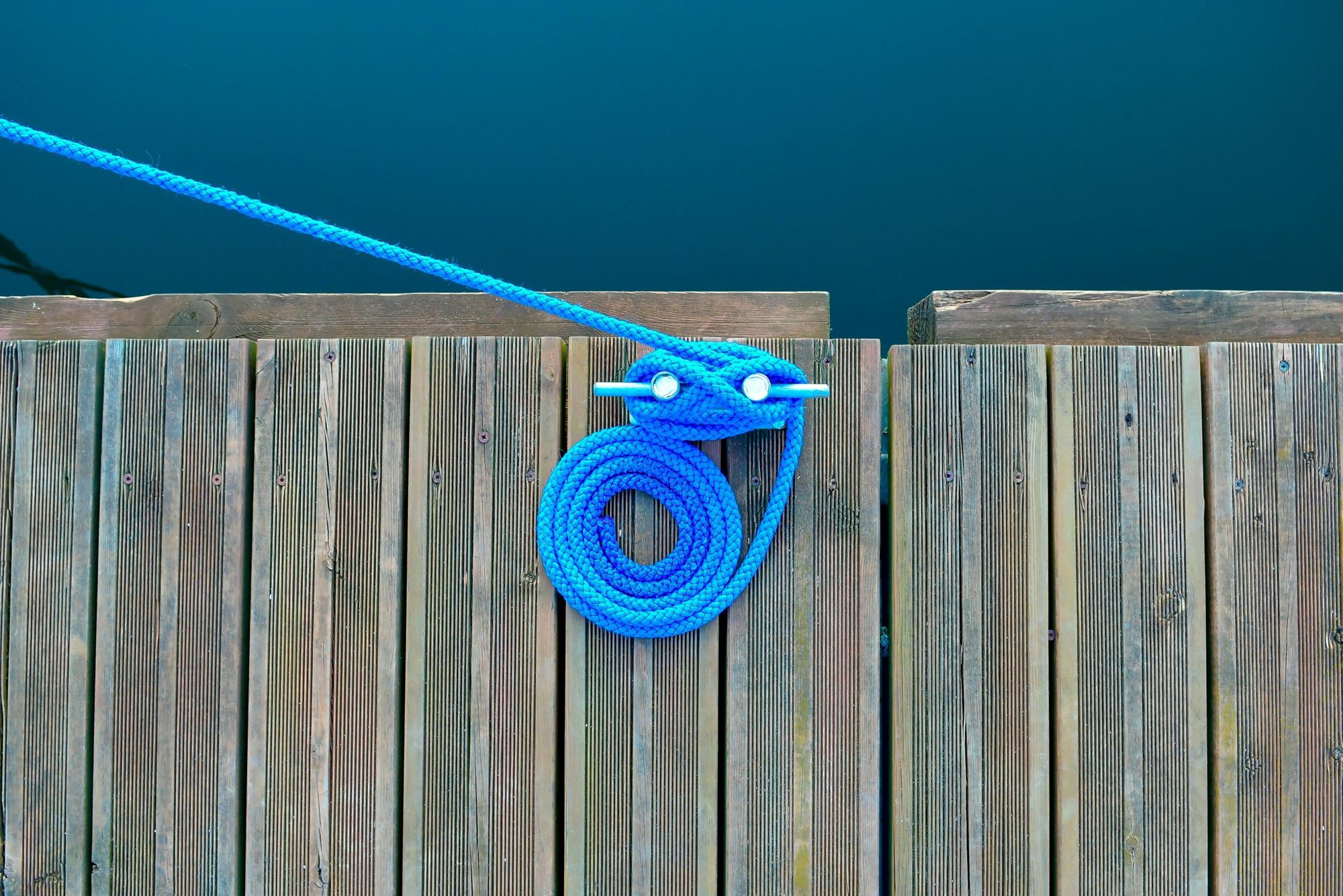 Bright blue dock line coiled around a cleat on a wooden dock