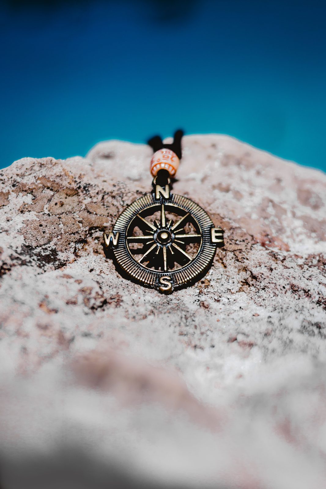 Brass compass rose pendant resting on a rock