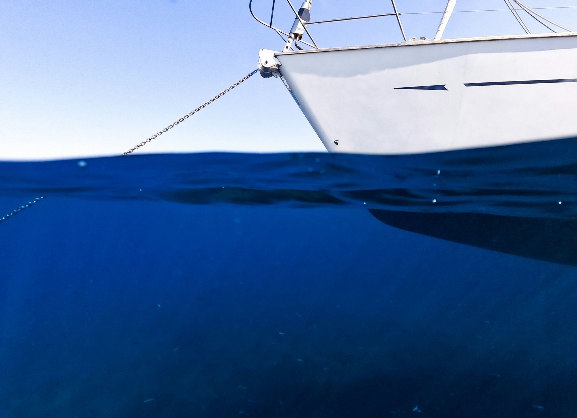 Bow of a sailboat at anchor, split view above and below the waterline with the anchor chain running into deep blue water