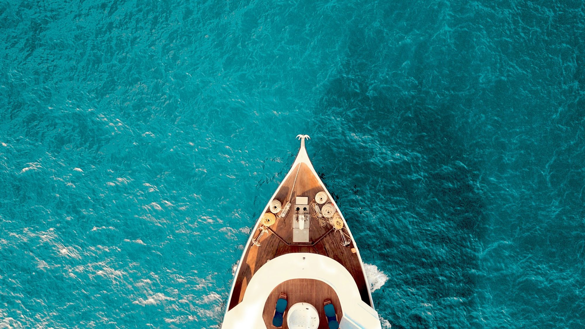 Bow of a boat cutting through deep turquoise water, seen from directly above