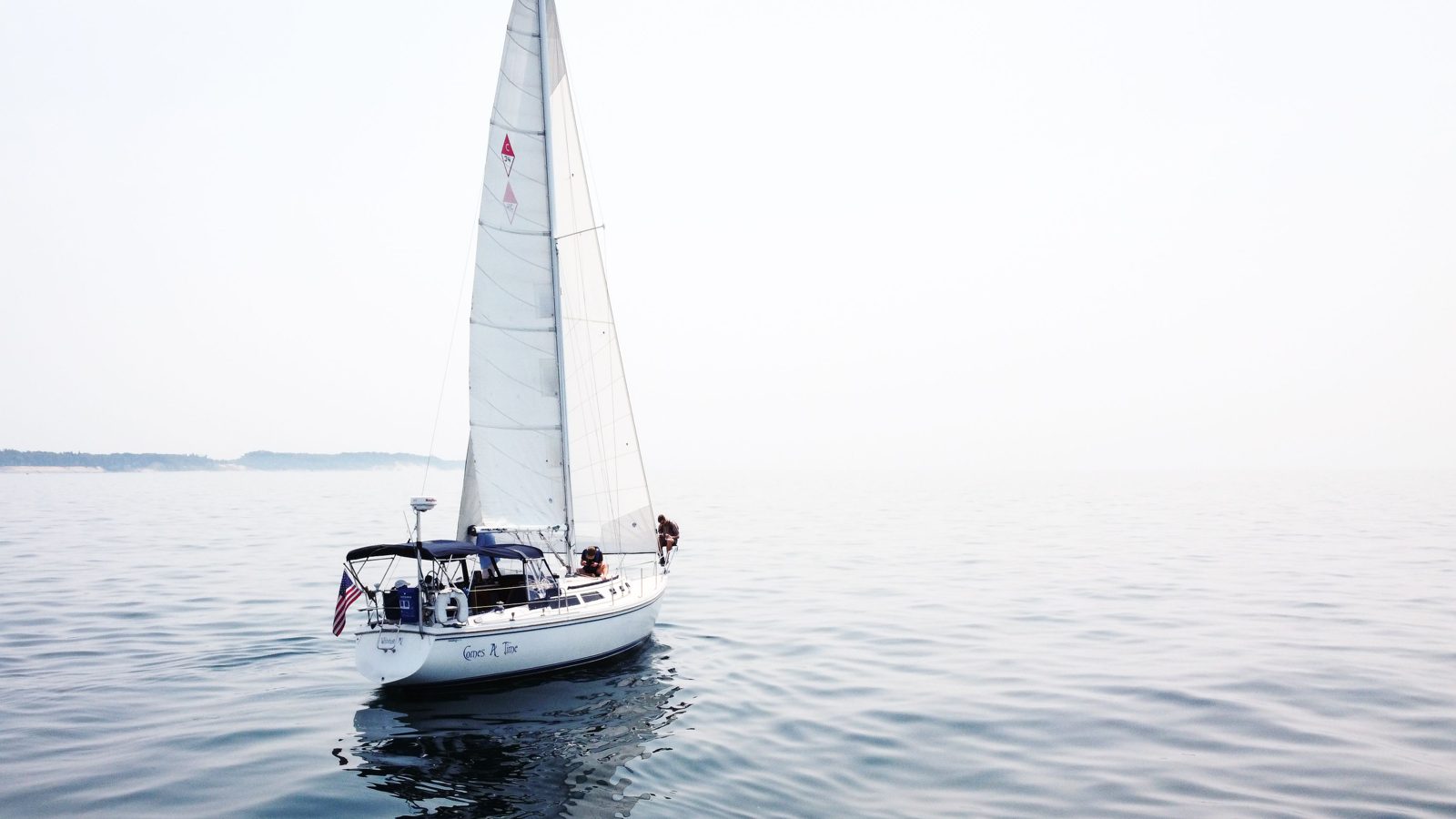 Sailboat under sail on flat, hazy water