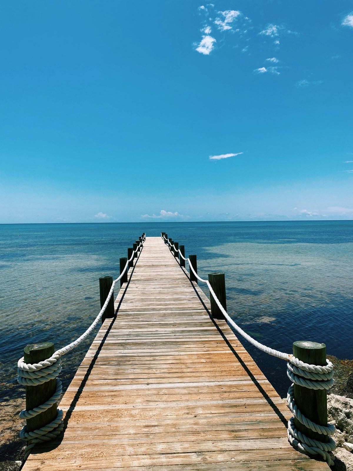 A wooden pier with rope rails running out to calm open water